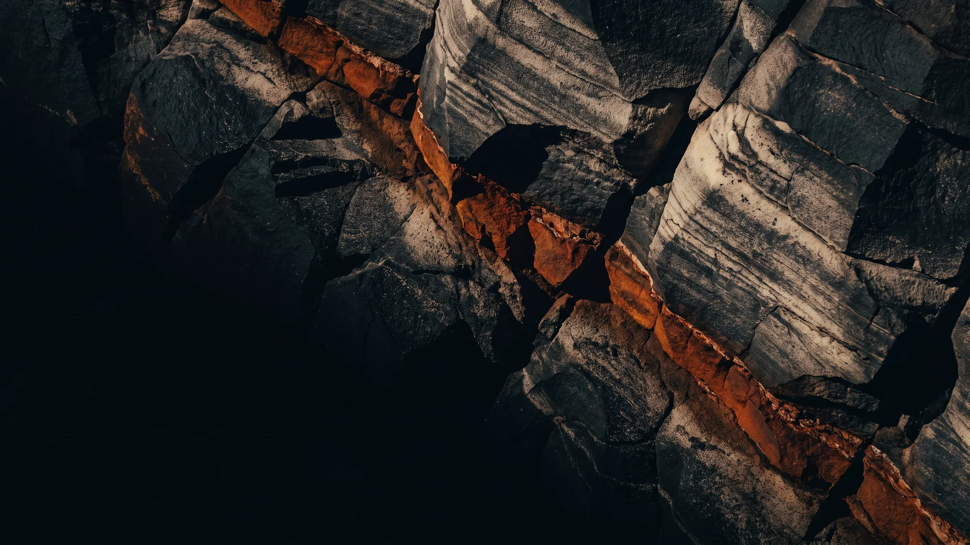 Conceptual study of fractured dark rock with a rust-colored mineral seam.